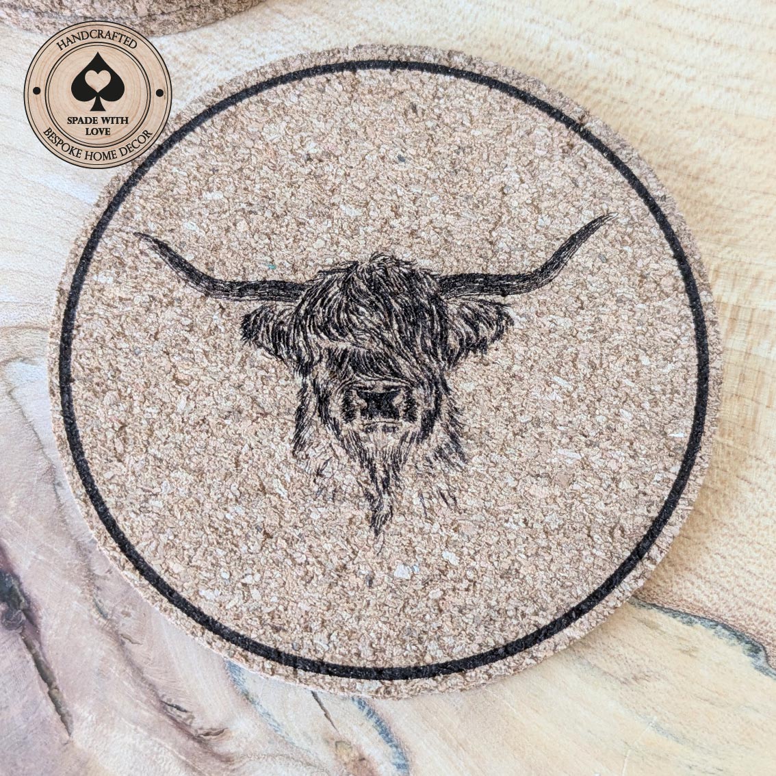 Round cork coaster with a highland cow design on a wooden surface.