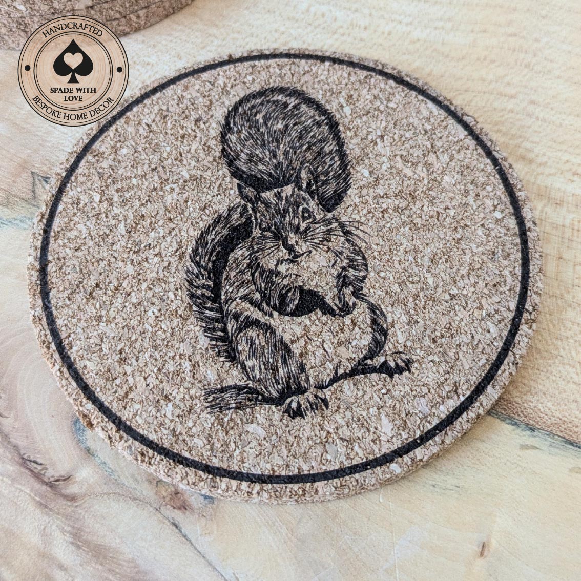 Round cork coaster with a squirrel design on a wooden surface, featuring the brand 'Handcrafted Spade with Love'.