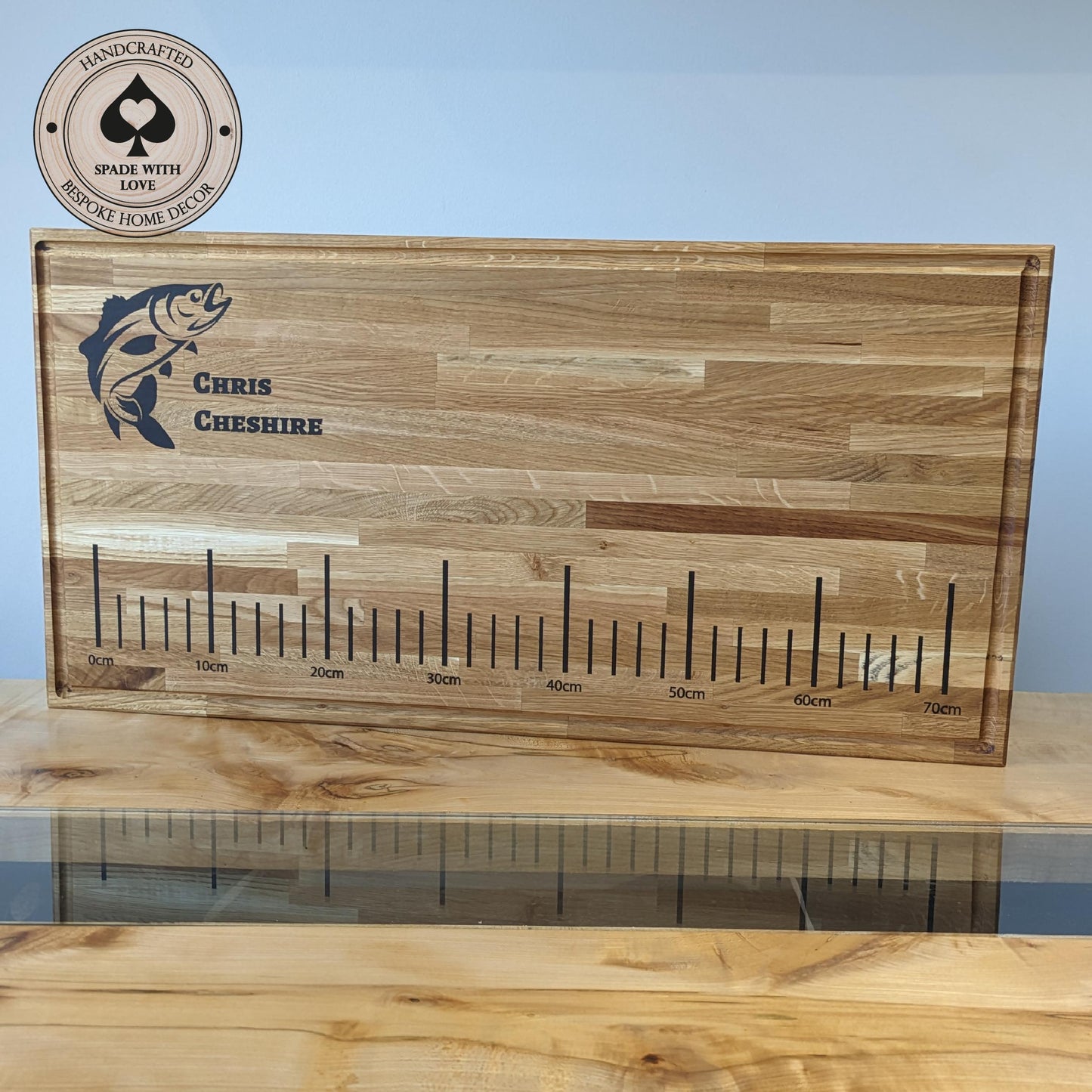 Wooden cutting board with engraved fish design and measurement scale on a blue background.