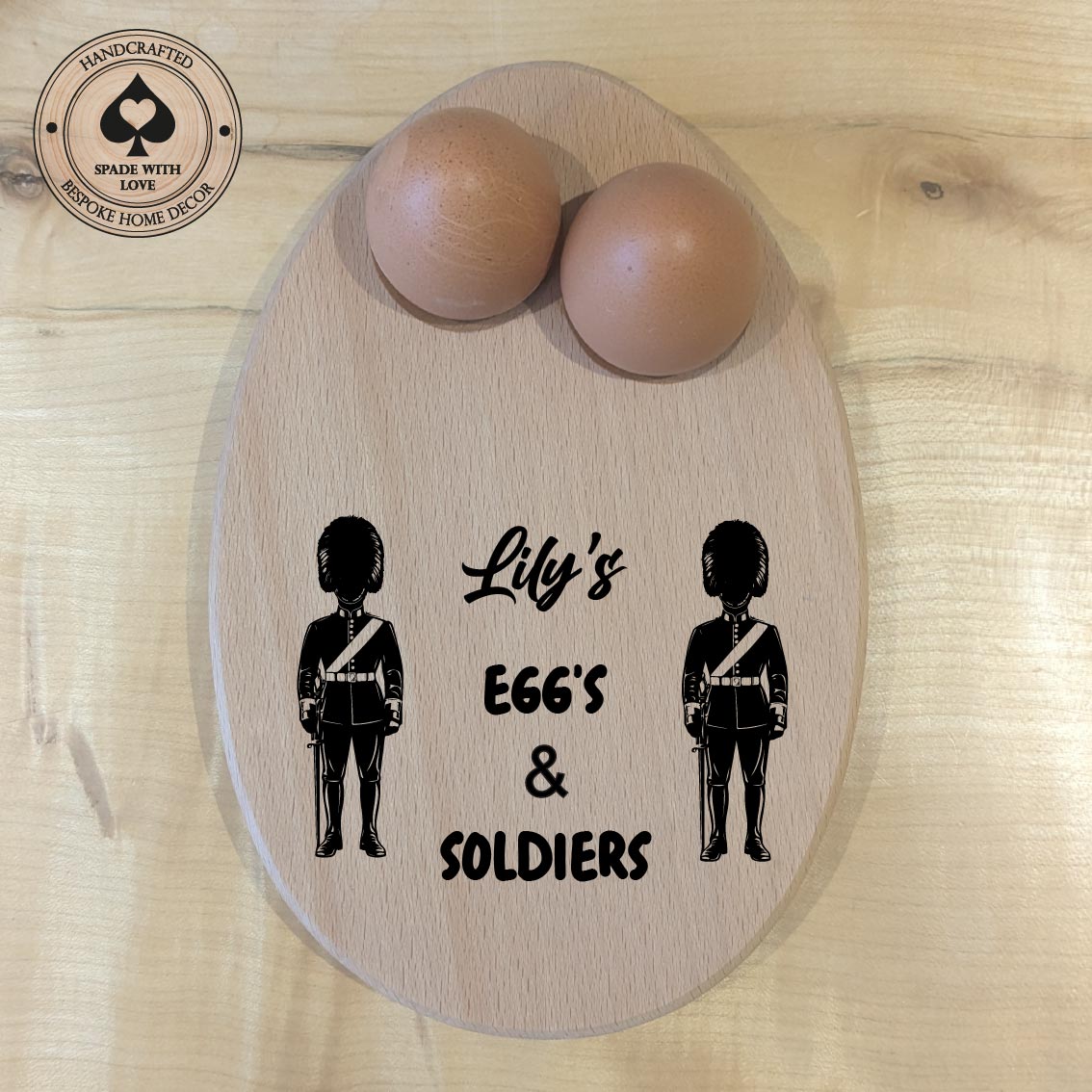 Wooden board with two wooden eggs and silhouettes of soldiers with text 'Lily's EGGS & SOLDIERS' on a wooden surface.