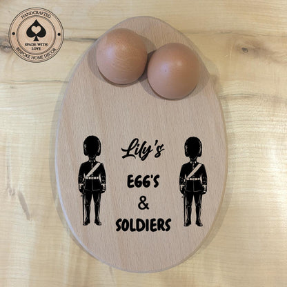 Wooden board with two wooden eggs and silhouettes of soldiers with text 'Lily's EGGS & SOLDIERS' on a wooden surface.